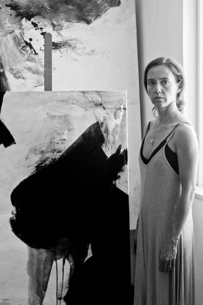 Portrait of Portuguese-English contemporary artist based in Lisbon, Portugal. Standing alongside her abstract paintings.